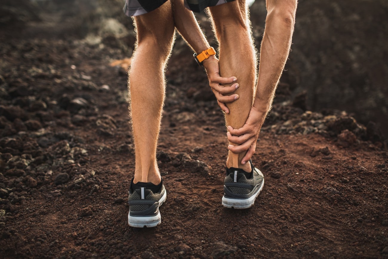 man stopping his run ona. dirt path holding his achilles tendon and heel in pain